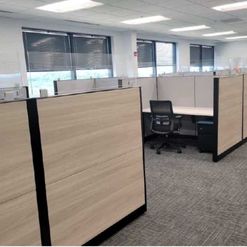Full office floor with light wood grain laminate cubicles, glass topper panels, and black trim frames